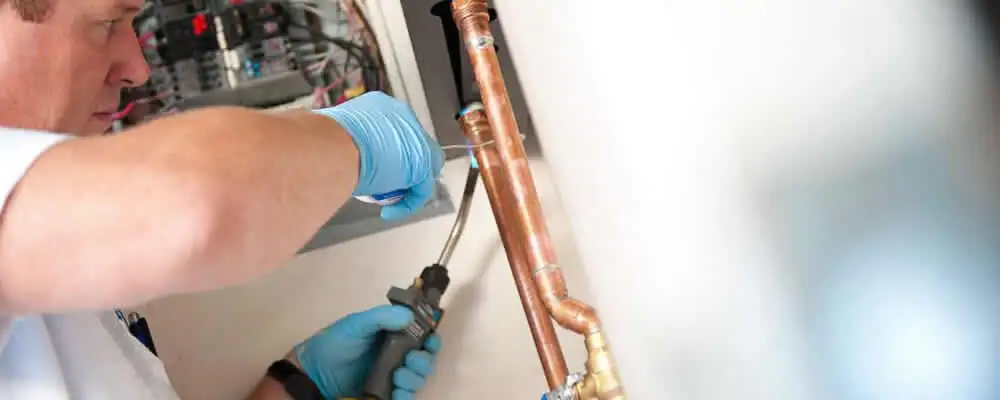 Water heater repair technician testing copper pipe connections and controls in Palm Springs, CA